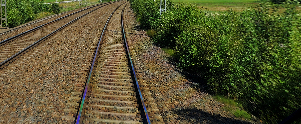 Två parallella järnvägsspår med grönska på sidorna.