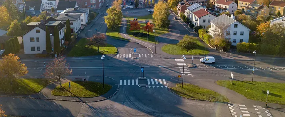 Korsning med gång- och cykelbanor samt övergångsställen. I bakgrunden syns en park med träd och gräs.