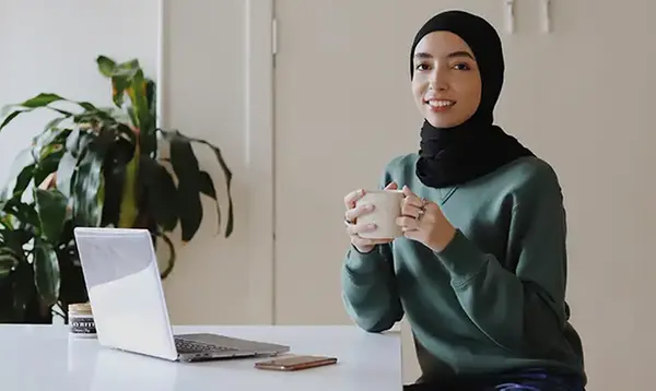 Kvinna med en kaffekopp i handen framför en dator